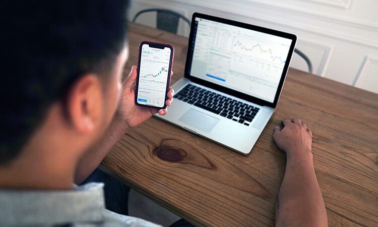 Man looks at investments on mobile and computer