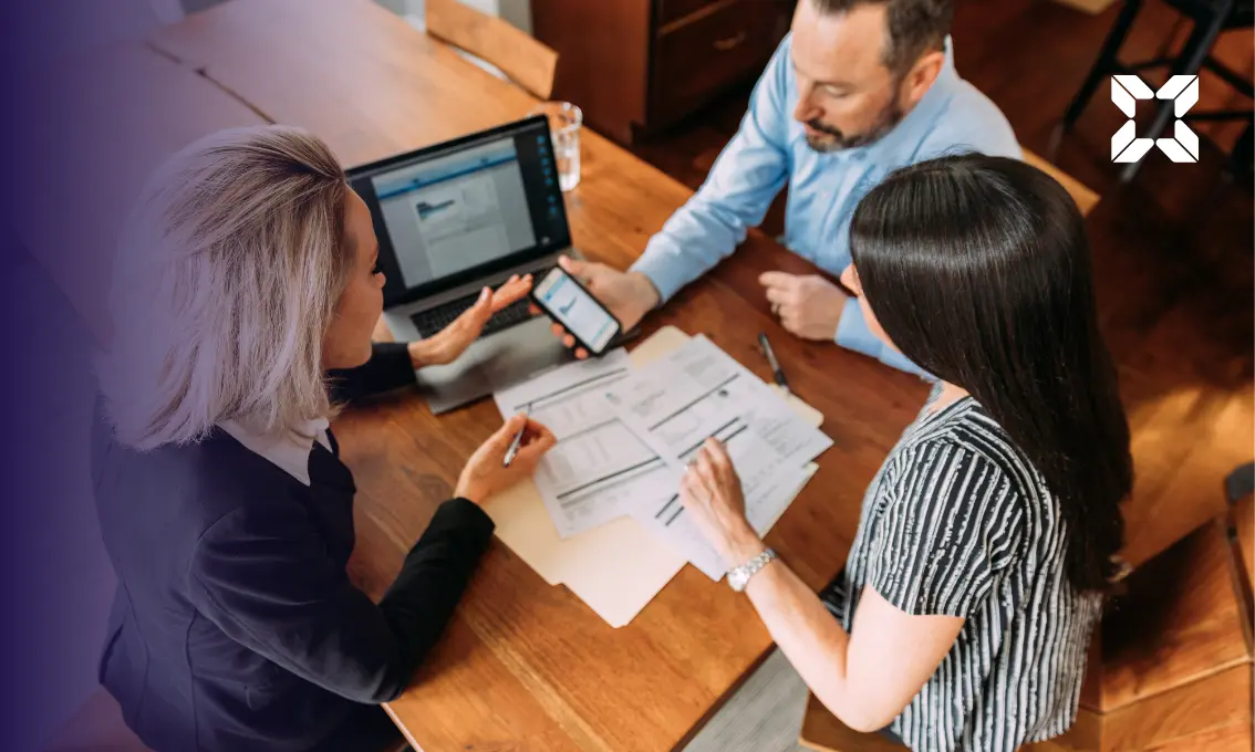 A couple sat around a table with an adviser looking at papers, a mobile phone and a laptop