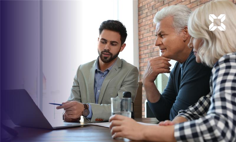 An older couple having something pointed out to them on a laptop screen by a younger adviser