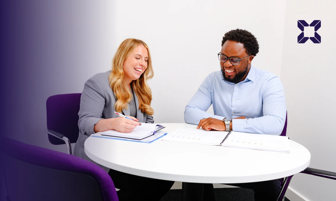 A male and female financial adviser are sat at a table having a discussion.
