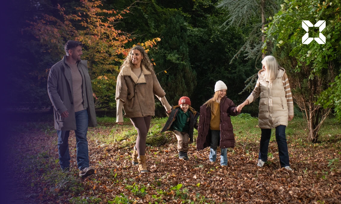 A family are walking through fallen leaves
